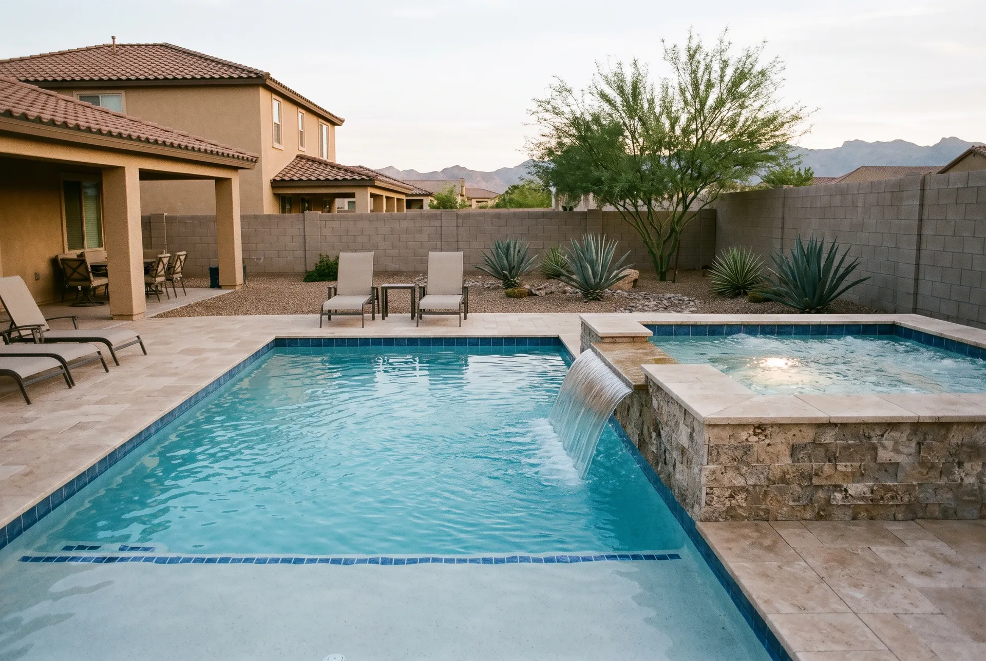 A new raised square spa with a stone veneer wall spilling a sheet of water into a rectangular pool, clear water, travertine deck